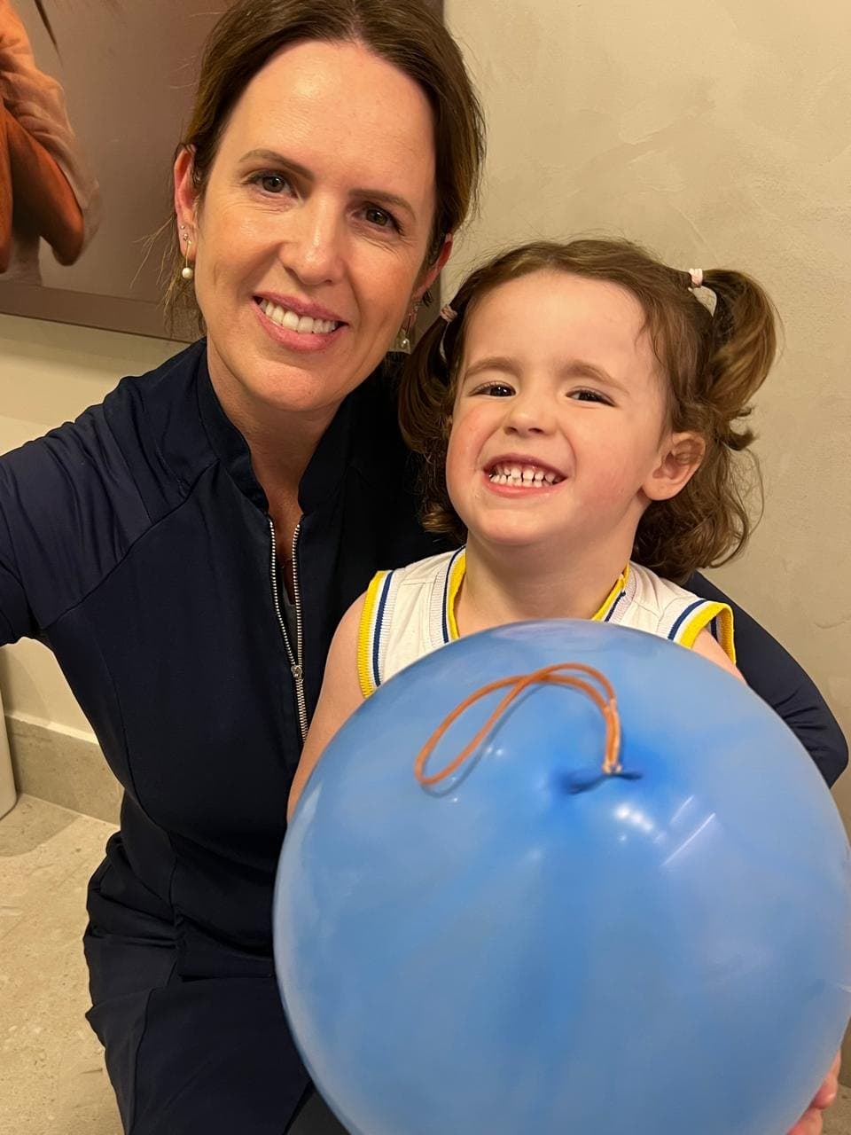 A dentista com uma pequena paciente sorridente segurando um balão azul